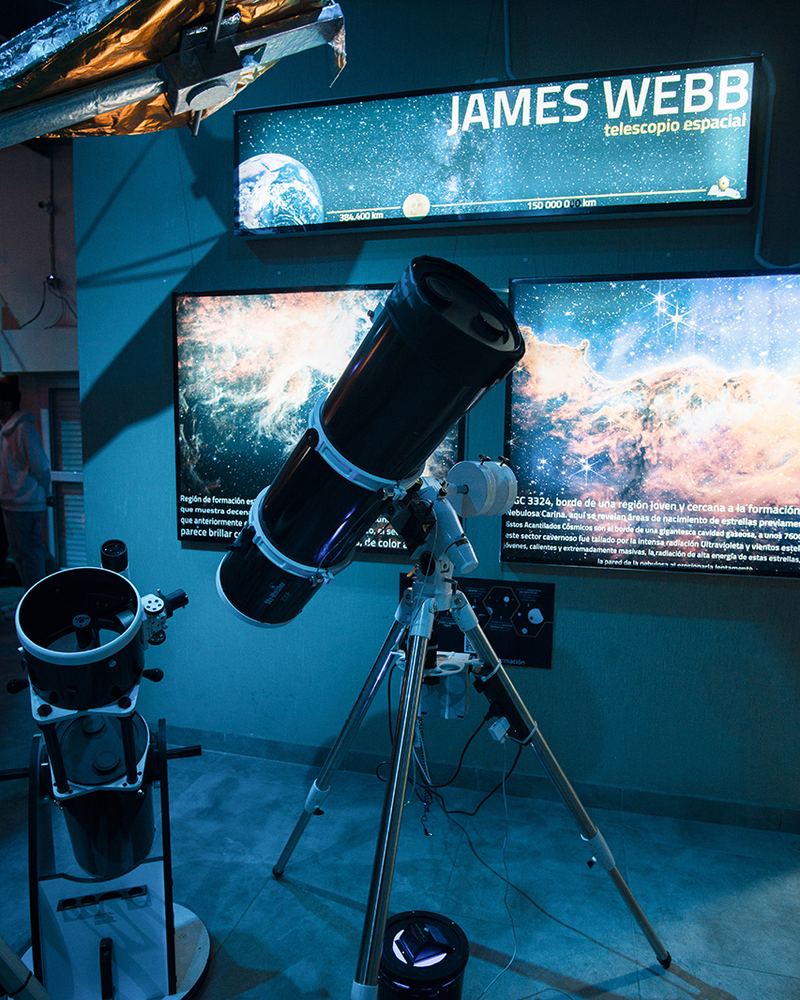 Telescopio frente a una pantalla con im&aacute;genes del telescopio espacial James Webb en el Planetario CIASIVE